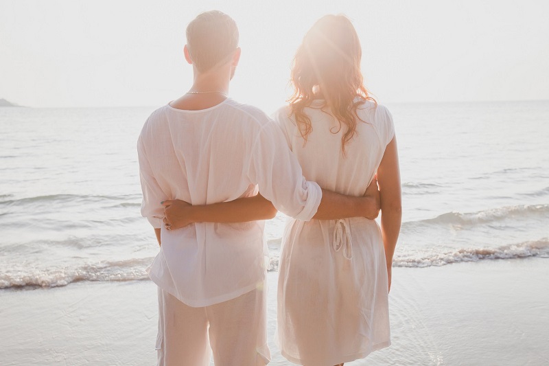 affectionate couple on the beach, honeymoon travel, rear view of man and woman standing together